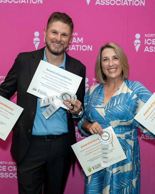 Two people holding awards in front of a pink background with logos.